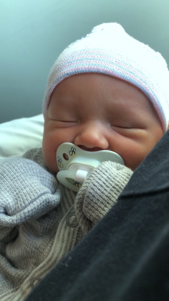 Newborn Luke asleep in a striped hospital hat with a pacifier, bundled in a knit outfit