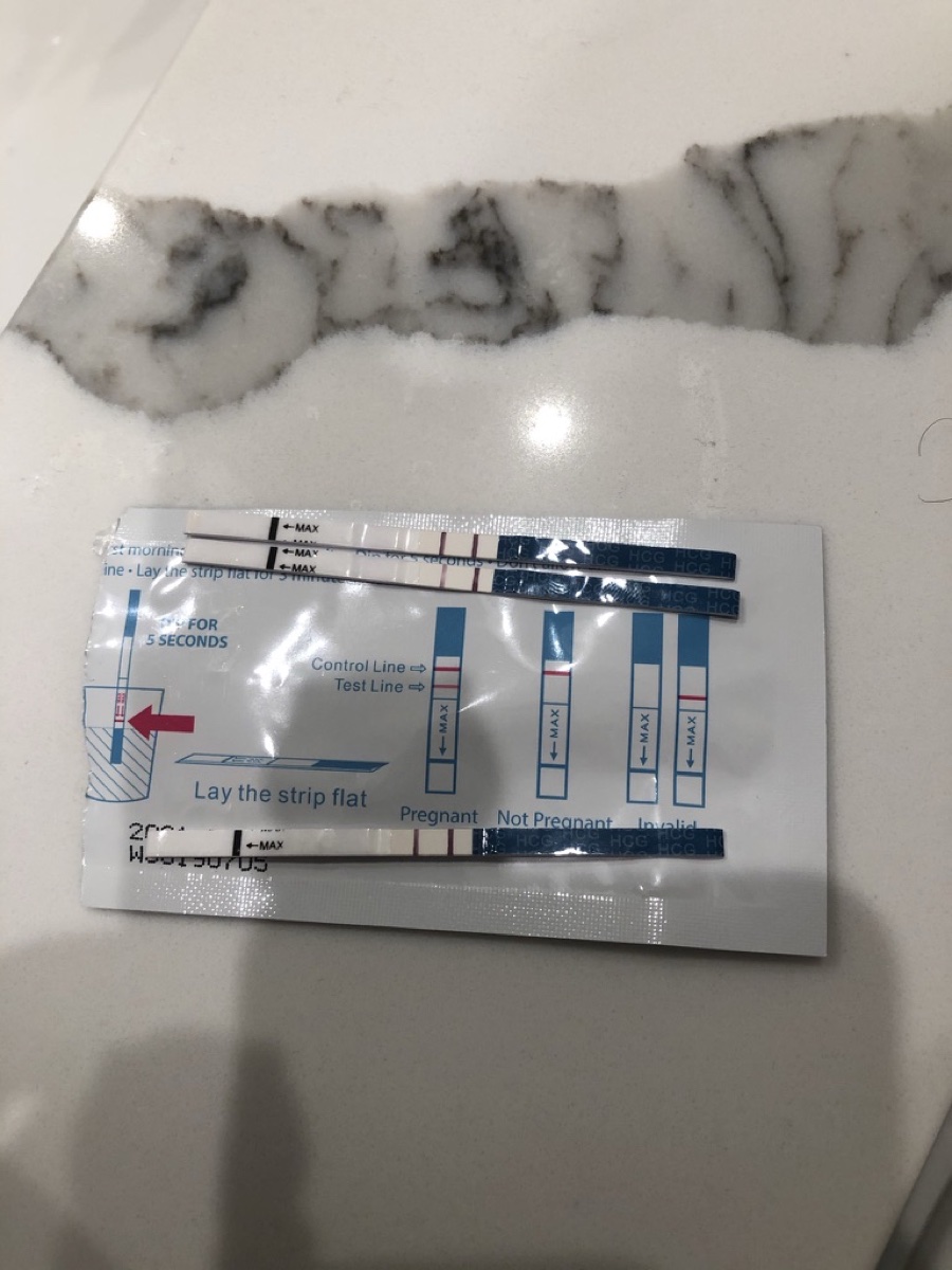 Three hCG test strips laid across their foil packet, each showing two red lines