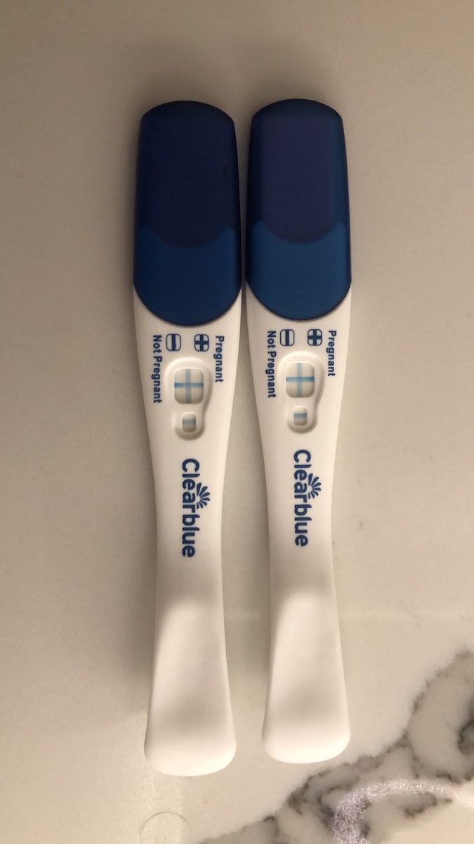 Two Clearblue tests side by side on the counter, each result window showing a blue plus